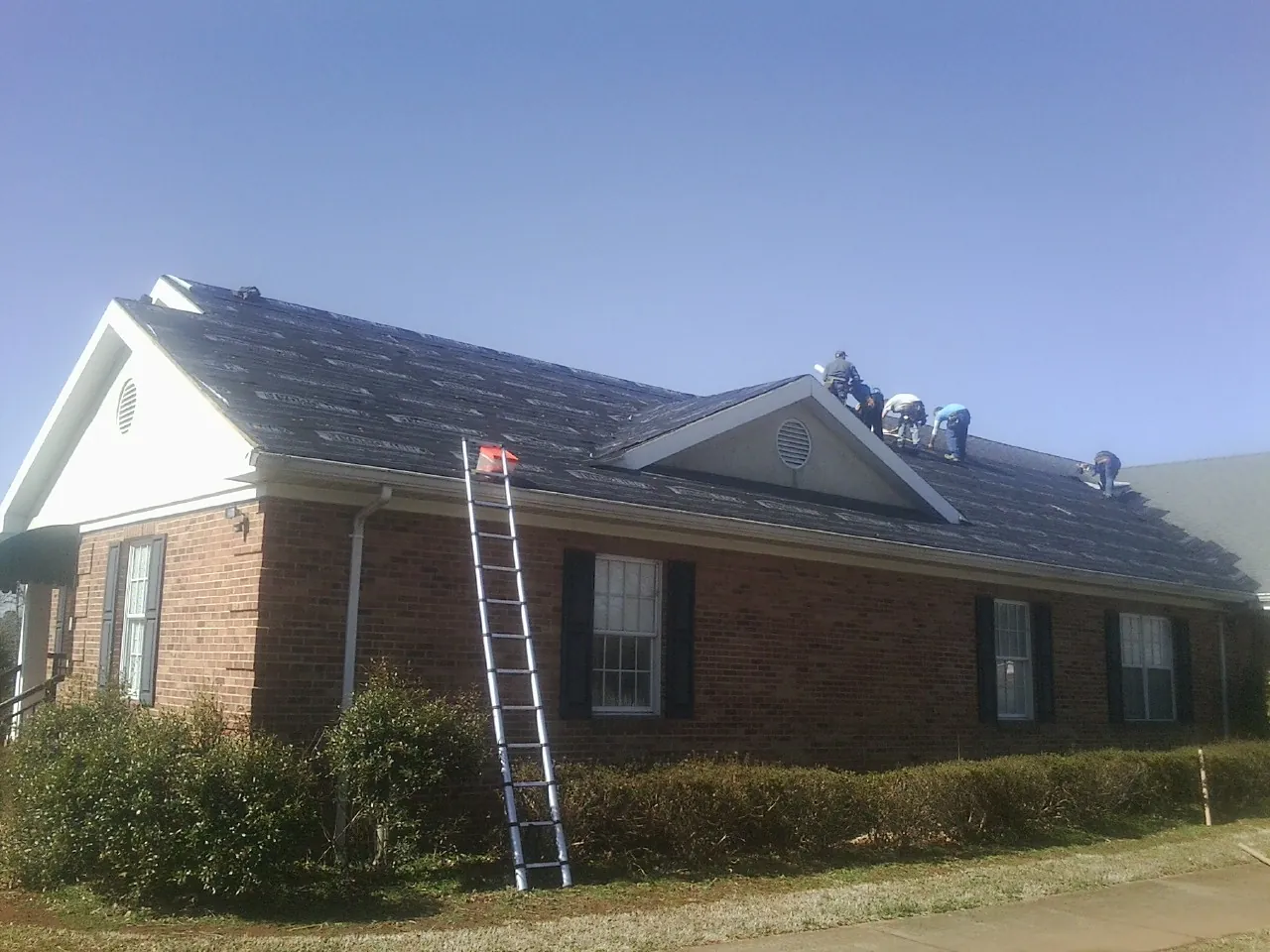 Crew tearing shingles off a brick ranch roof with a ladder set — Metal Roof Repair work by our crew in Dresher