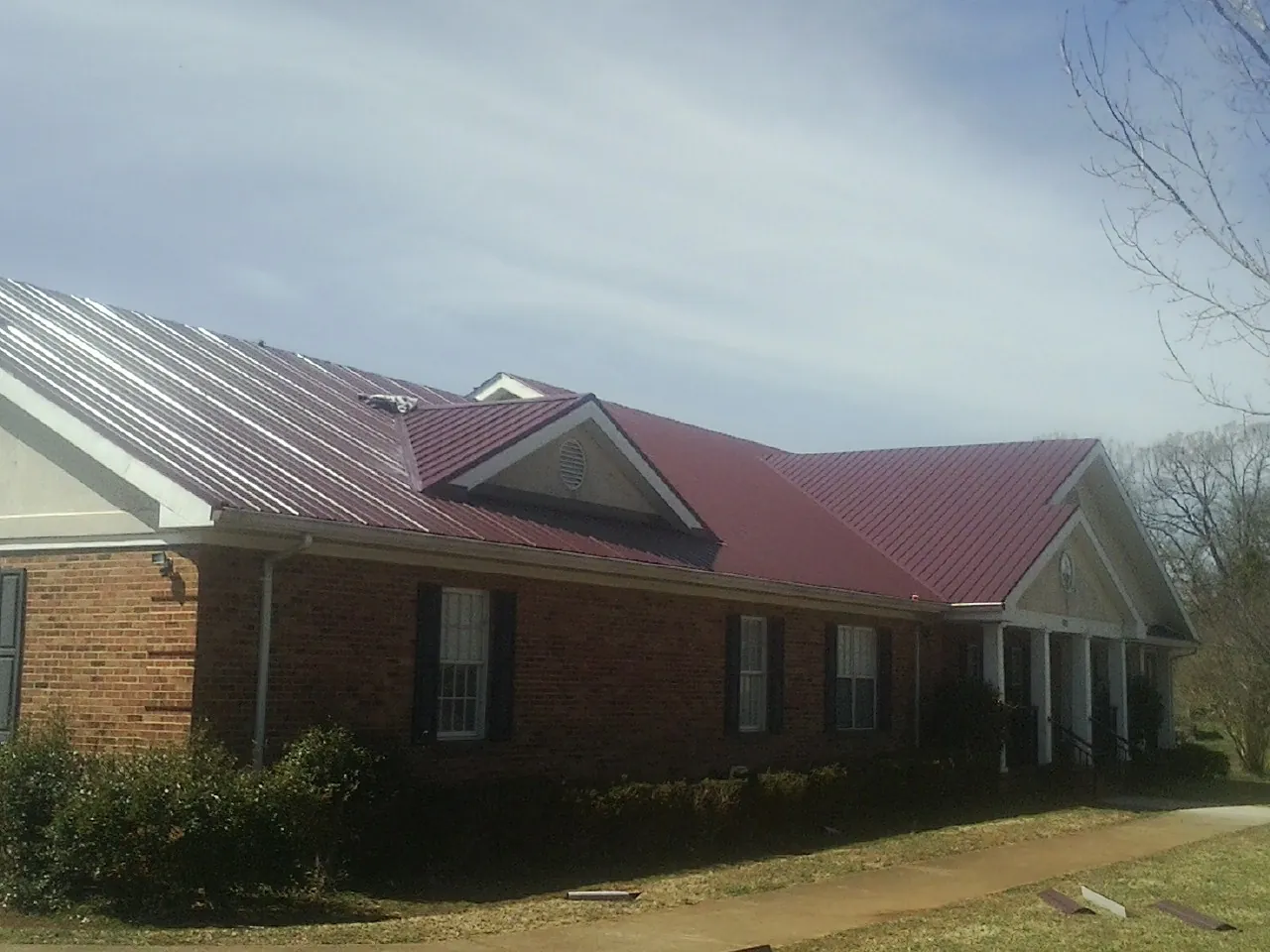 Red metal roof with gabled entries on a long brick building, from a Hail Damage Roof Repair job in Dresher