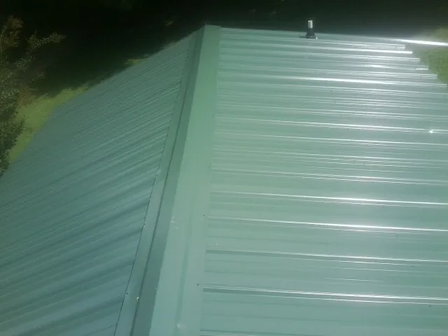 New green metal panels meeting at the ridge of a roof — Flat Roof Repair work by our crew in Dresher