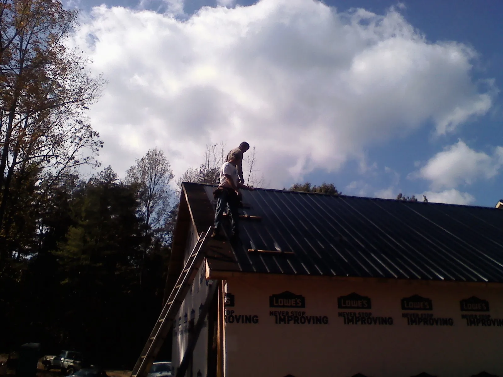 Roofer fastening dark metal panels high against a cloudy sky, from a Roof Inspection job in Dresher
