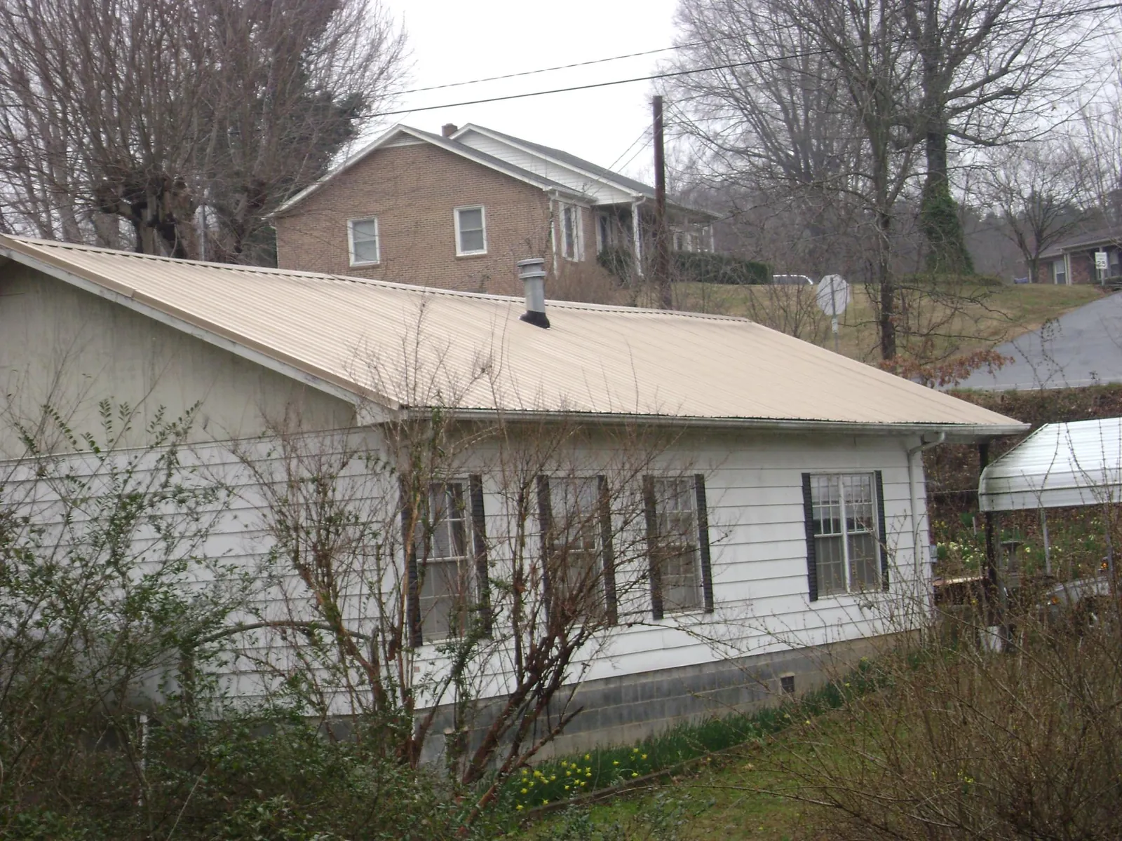 Tan metal roof on a white sided house set into a hillside — Commercial Roofing by Roofing Brothers in Dresher
